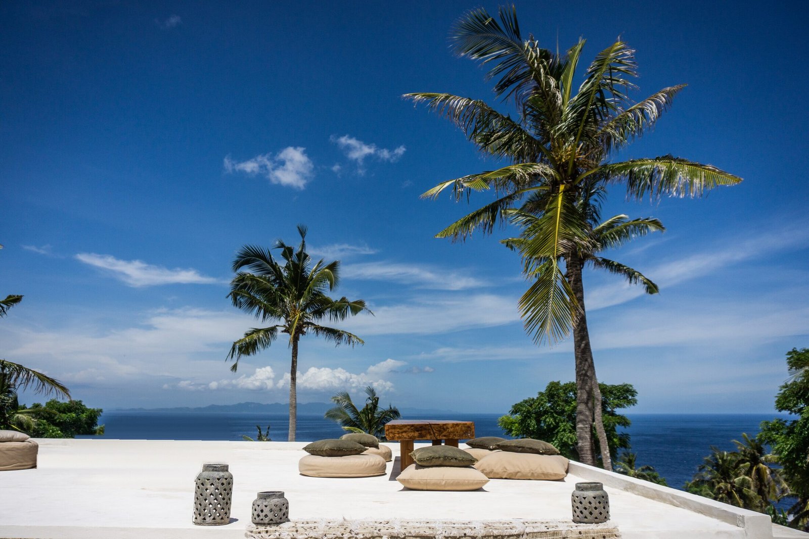The ocean-view terrace at Raja Lima on a sunny day, with palms and floor cushions