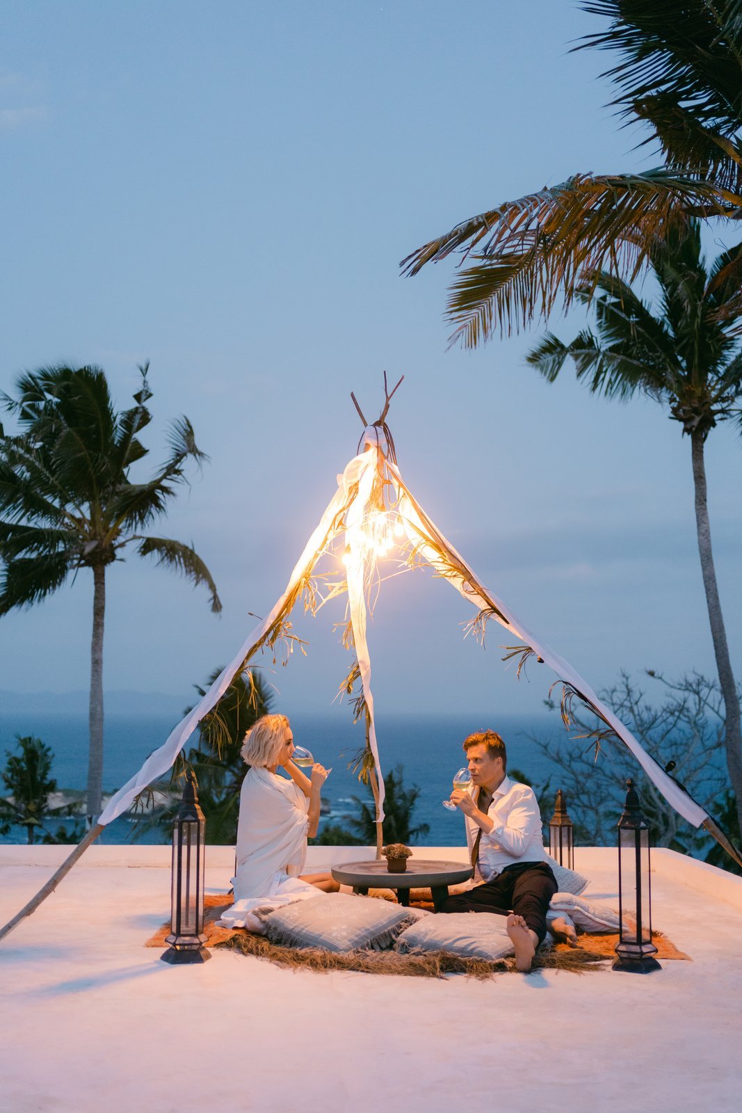 A couple sharing a drink under a lit tipi on the terrace at dusk
