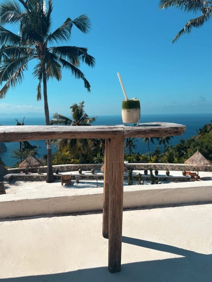 An iced matcha latte on a wooden bar above the ocean